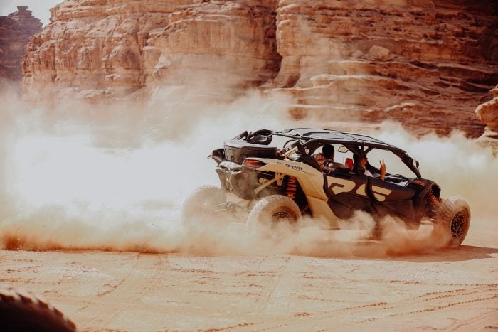 Two men driving a luxury quad desert car in the sum in the desert around large rocks