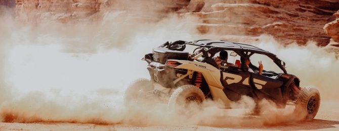 Two men driving a luxury quad desert car in the sum in the desert around large rocks