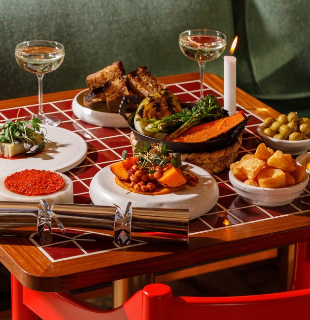 Christmas dinner small plates and martini glasses of champagne displayed on a squared red and white checkerboard table and chairs.