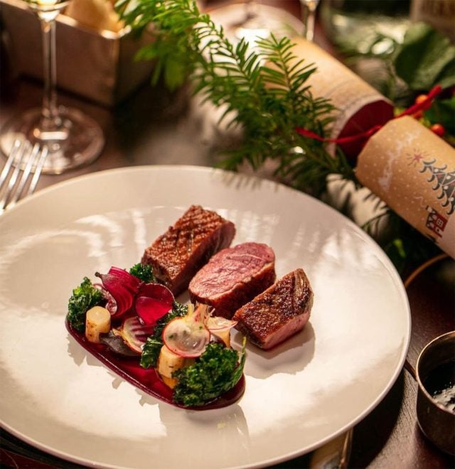 Steak and vegetable garnish in a rounded white plate next to a Christmas cracker.