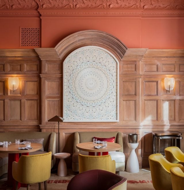 Interior restaurant with colourful comfy chairs, rounded small tables and wooden paneled archway walls with ceramic wall display.