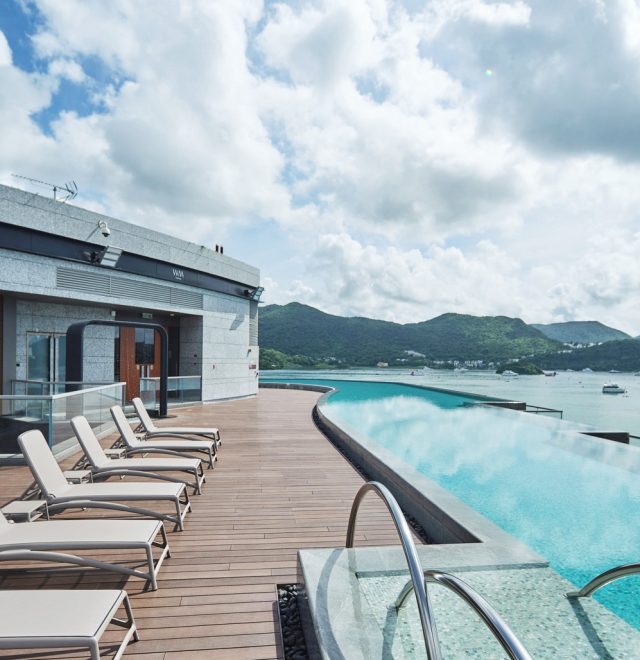 Outside luxury pool with a row of sunbeds on decking overlooking the coat