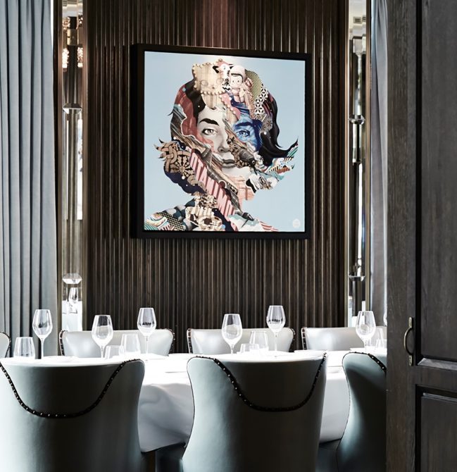 Inside restaurant with table setting and chairs facing a paneled wall with abstract portrait of a women.