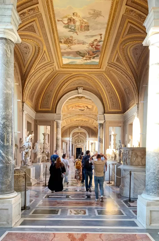 Inside the Vatican with huge ceilings covered in paintings and large pillars between sculptures