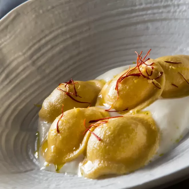 Tortellini pasta served in deep white bowl with sauce and red garnish